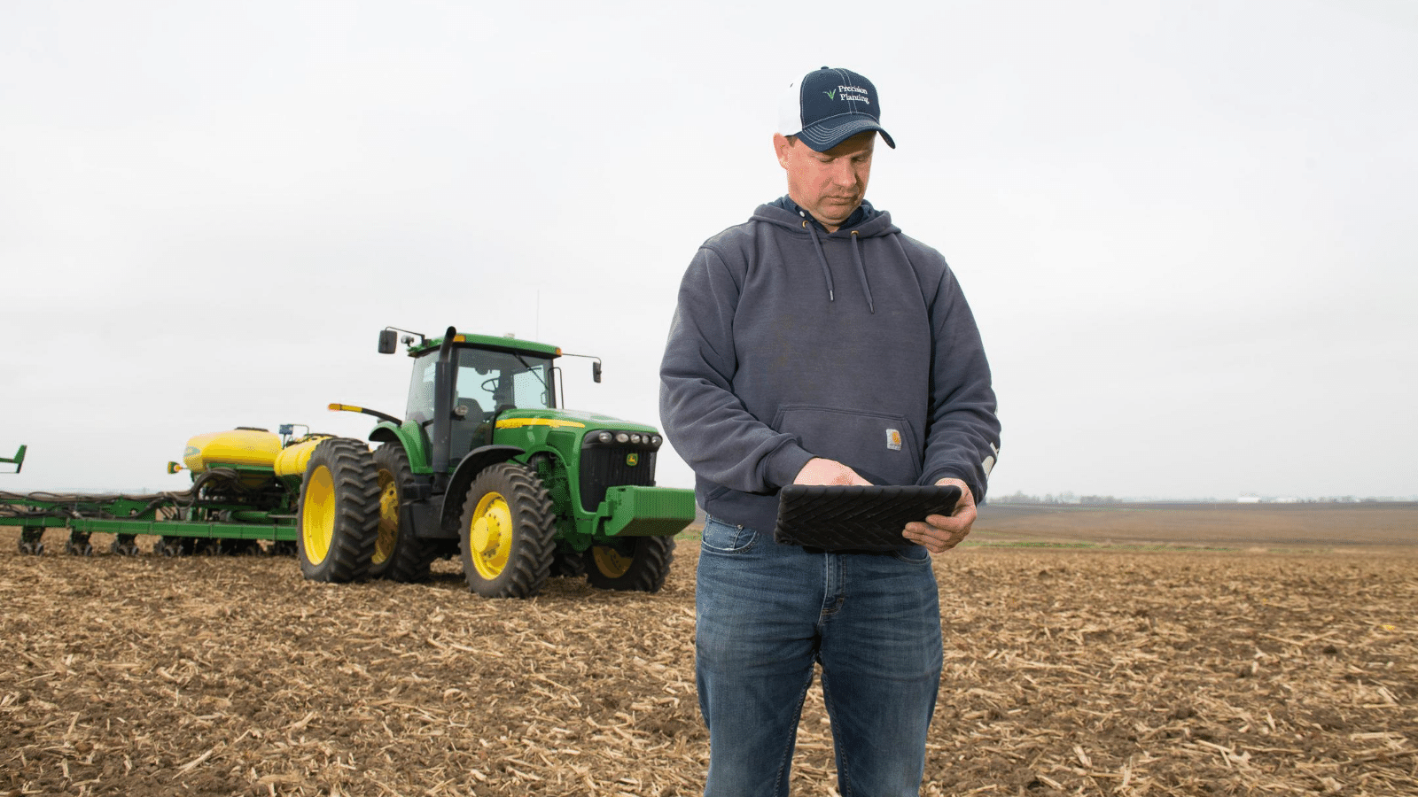 A farmer stands in his field looking at data on his tab