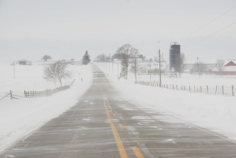 Snow blows over a rural road.