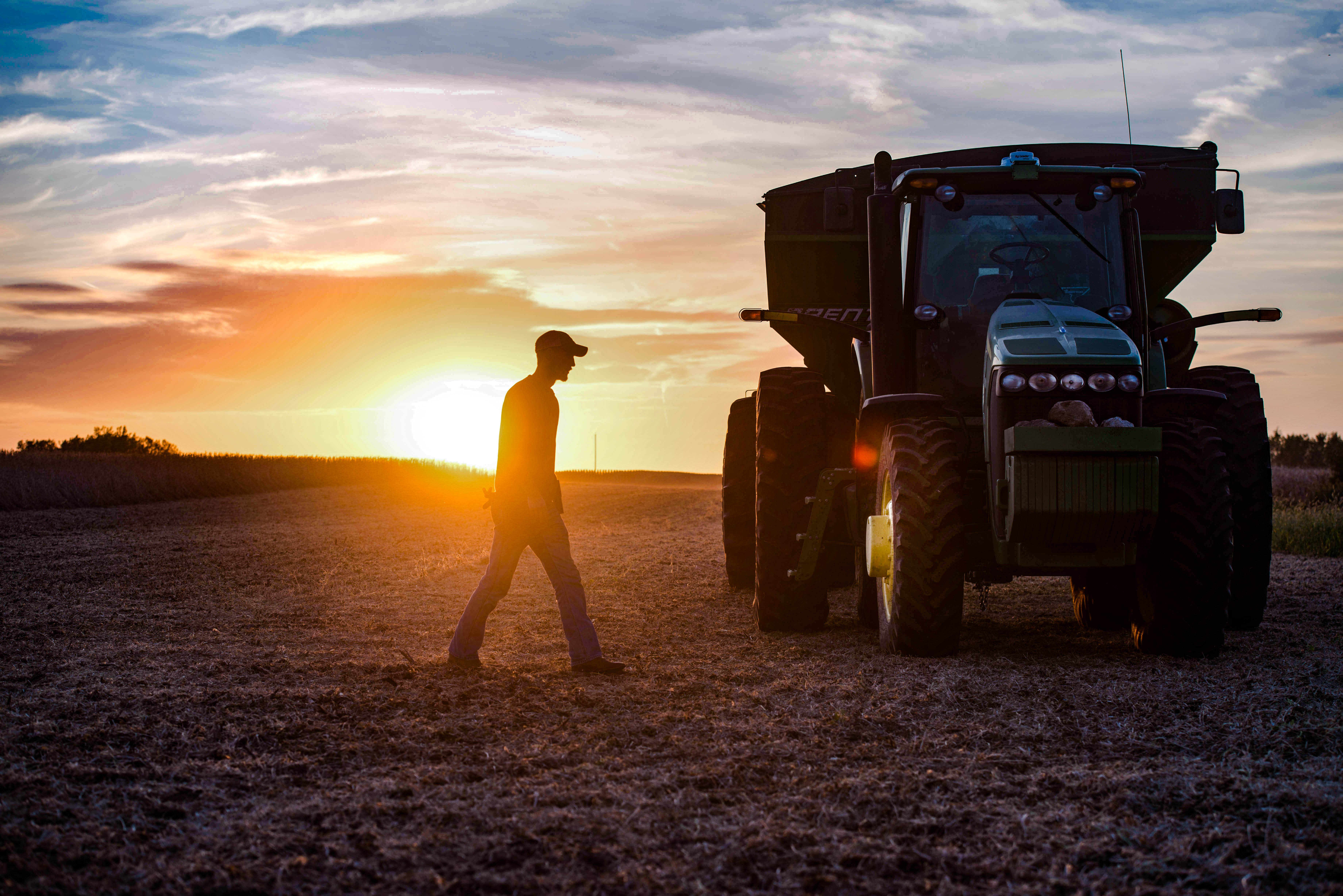 The silhouette of a farmer and tractor can be seen duri