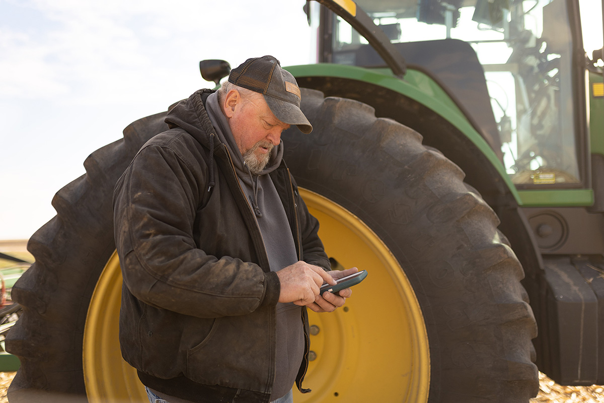 Farmer checking cell phone by John Deere tractor