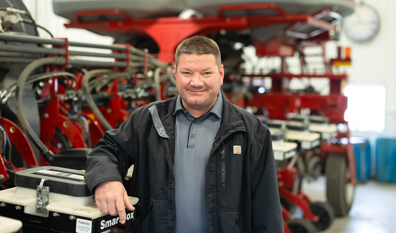Farmer standing next to planter in shop.