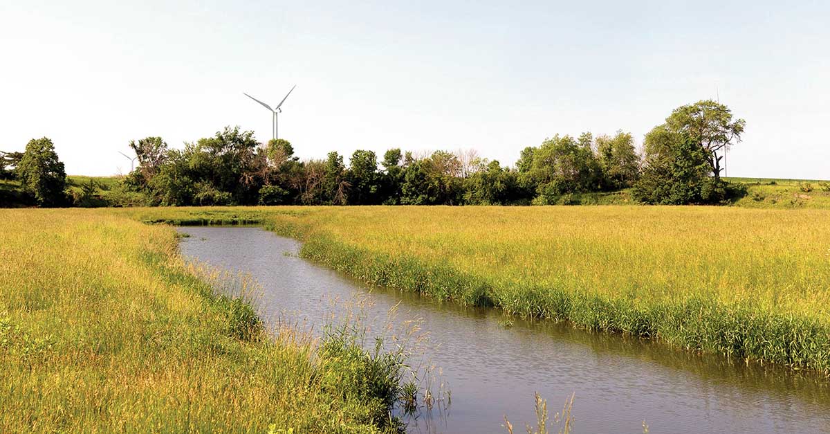 Water flowing through grass field with wind turbine in 
