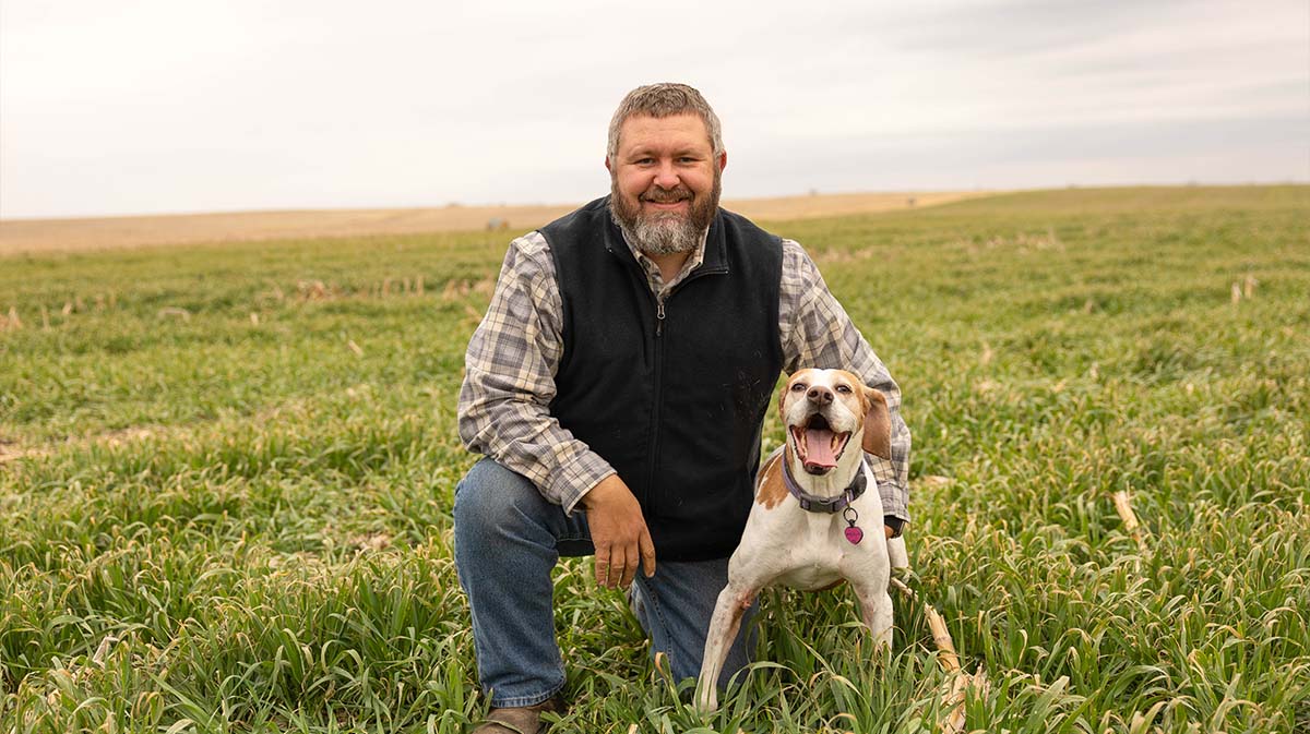 Farmer kneeling in field with his dog