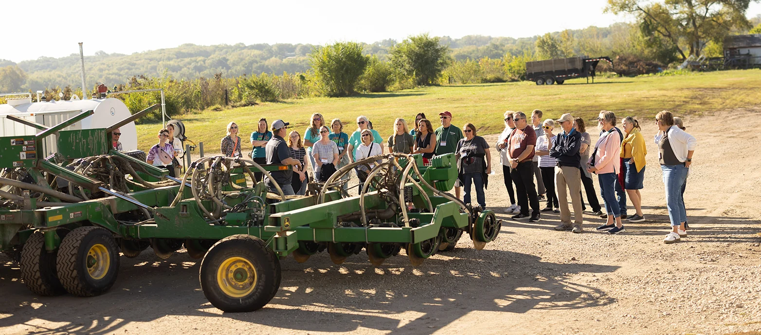 A Crowd Stands in Front of Farm Machinery 