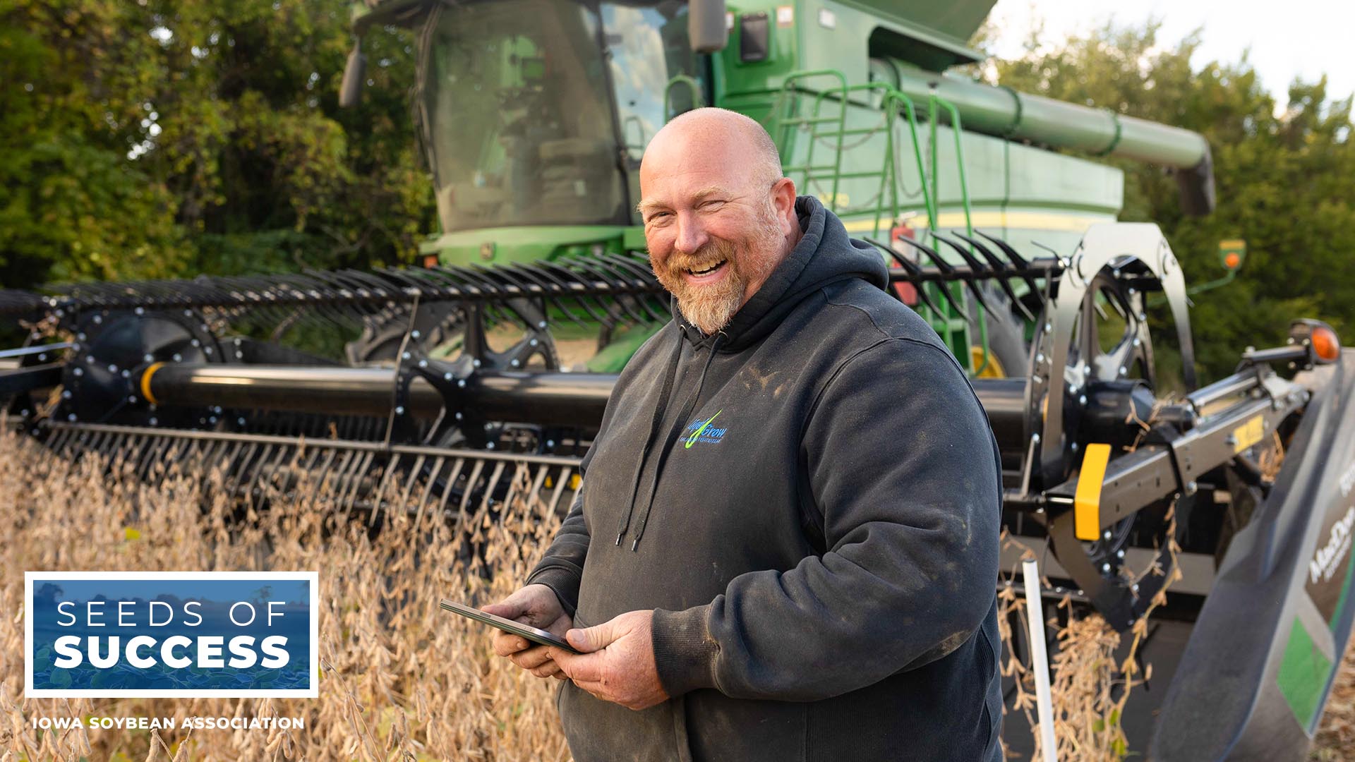 Farmer stands in front of John Deere combine holding iP
