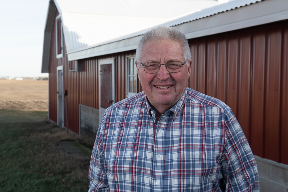 Hubert poses for a photo in a plaid shirt in front of h