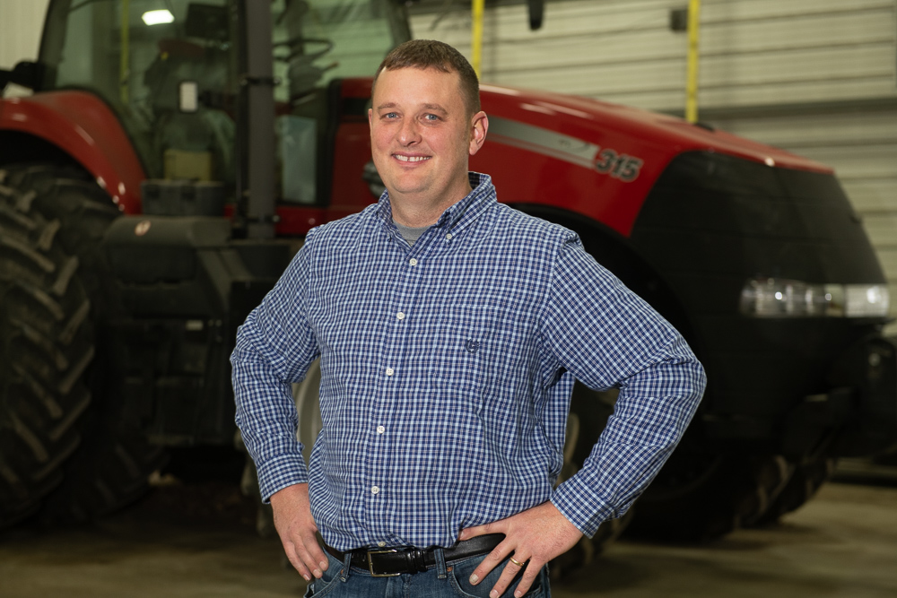 Mike Coleman poses in a plaid shirt in front of his red